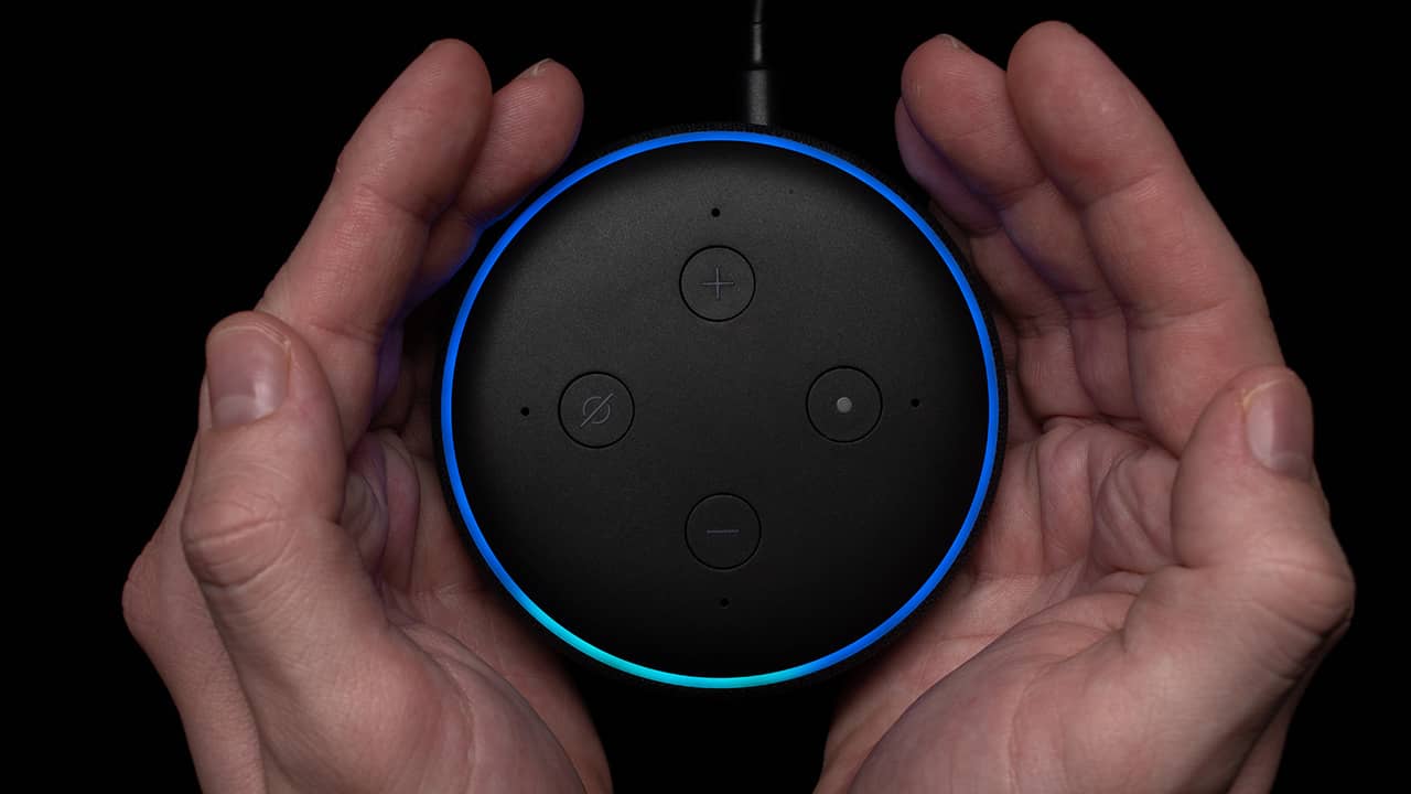 Two cupped hands holding an Echo Dot whose top edge glows blue and cyan against a black background